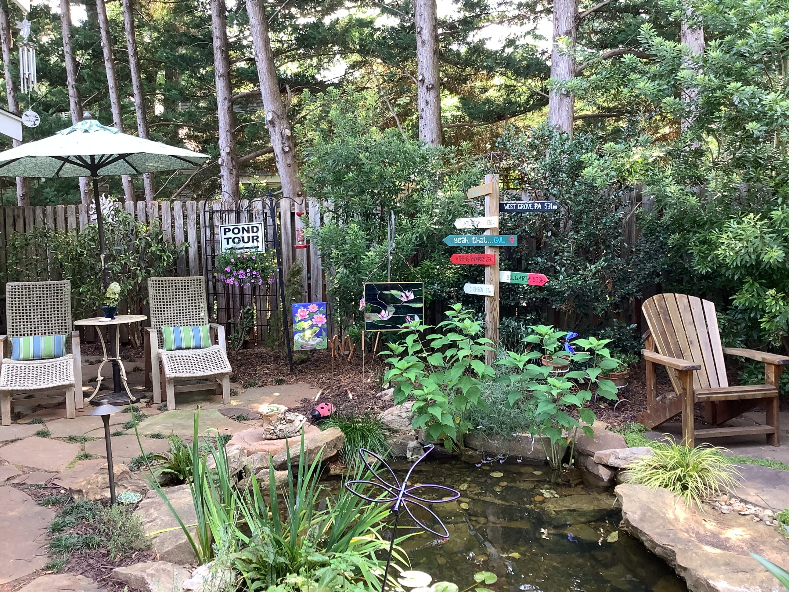 A garden with chairs, pond and trees.